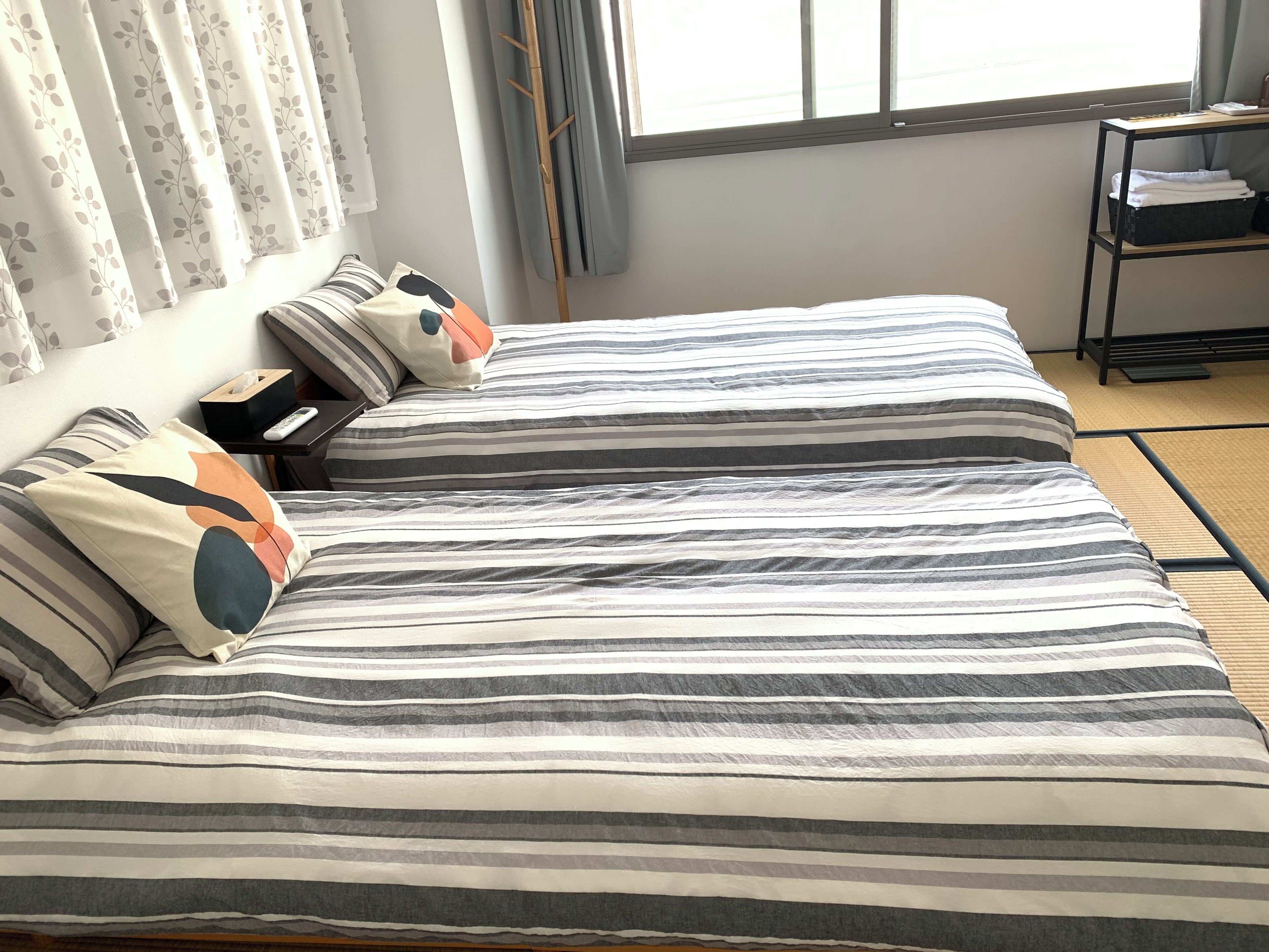 A double bed with striped bedding, a bedside table with a remote control, and a window with curtains.