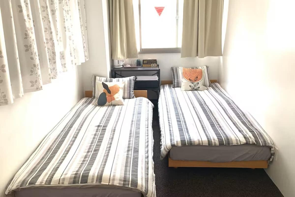 A room with two beds, a desk, and a window with curtains.