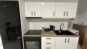 A compact kitchen with a black refrigerator, a stove, a sink, and white cabinets. - Loutra Suites Spring Breeze Studio (Corinth)