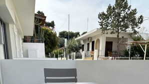 An outdoor patio with a table and two chairs, a tiled floor, and a building in the background. - Loutra Suites Spring Breeze Studio (Corinth)
