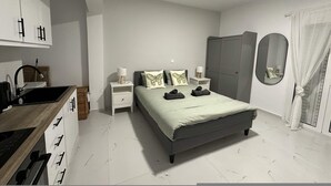 A modern bedroom with a bed, bedside tables, a wardrobe, and a bathroom with a mirror. - Loutra Suites Spring Breeze Studio (Corinth)