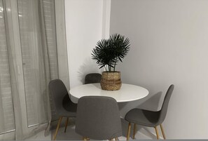 A dining area with a round white table, four grey chairs, and a woven basket with a plant. - Loutra Suites Thermae Garden Suite (Corinth)
