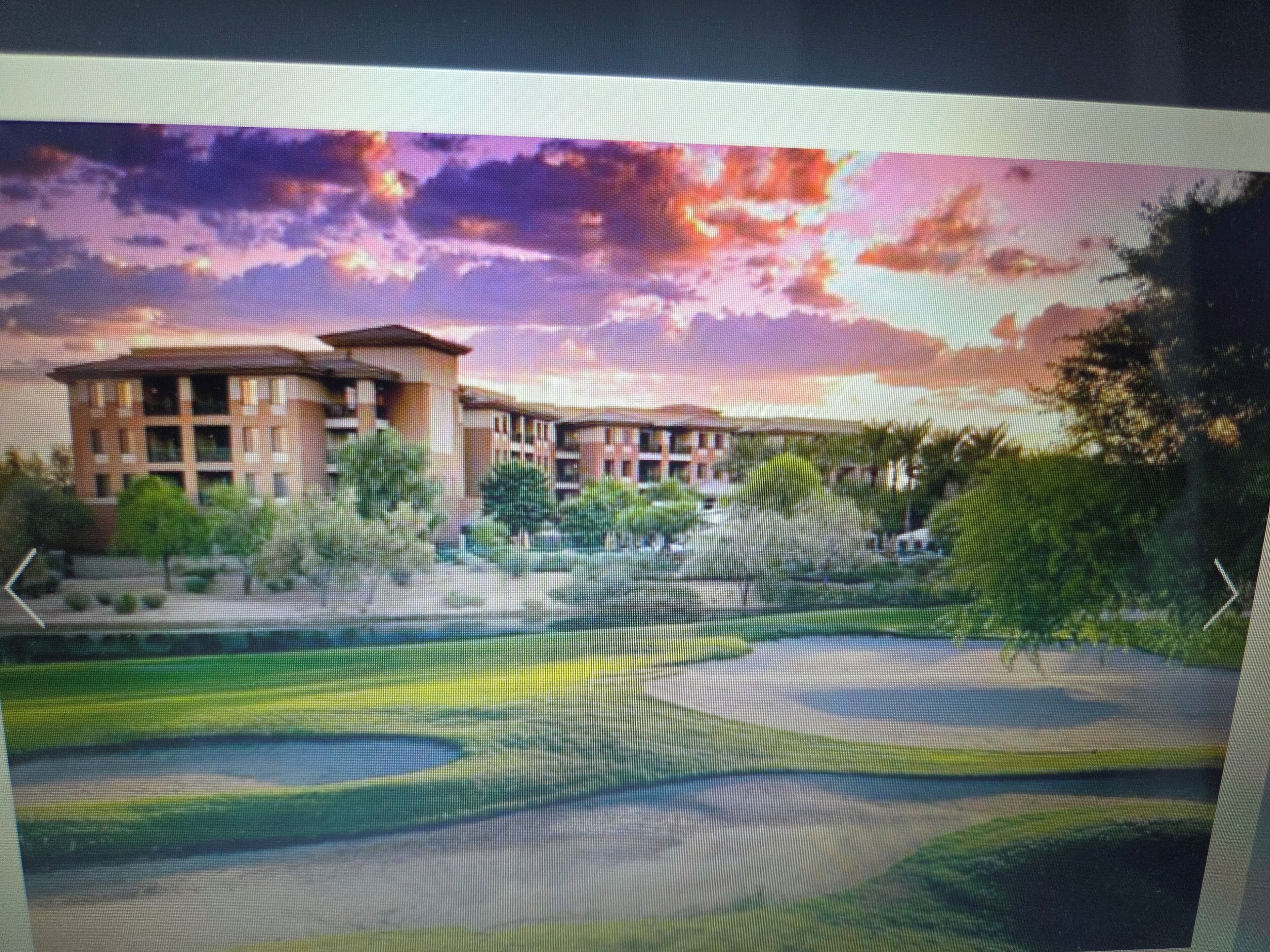 A modern building with multiple floors, surrounded by greenery and a golf course.
