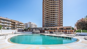 A hotel with a large pool, a tall building in the background, and a clear blue sky. - Apartment 'Praia Azul Ocean View' with Sea View, Wi-Fi and Air Conditioning (Portimão)