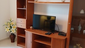 Una sala de estar con televisor, mueble de madera para entretenimiento y un jarrón con flores.