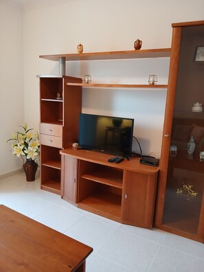 Ein Wohnzimmer mit Fernseher, einem Holz-Entertainment-Möbel und einer Vase mit Blumen.