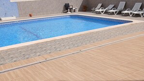 Una piscina con borde de azulejos, una terraza soleada con un desagüe y sillas de descanso junto a la piscina.