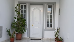 Una entrada limpia y luminosa, con suelo de mármol, una puerta blanca y plantas en macetas a ambos lados.