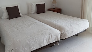 Una cama doble con colcha estampada, dos almohadas, una mesita de noche con lámpara, y dos cuadros en la pared.