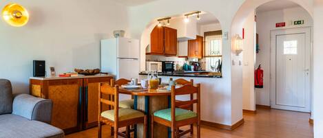 A modern kitchen with wooden cabinets, a dining area with a table and chairs, a sofa, and a hallway with an archway.