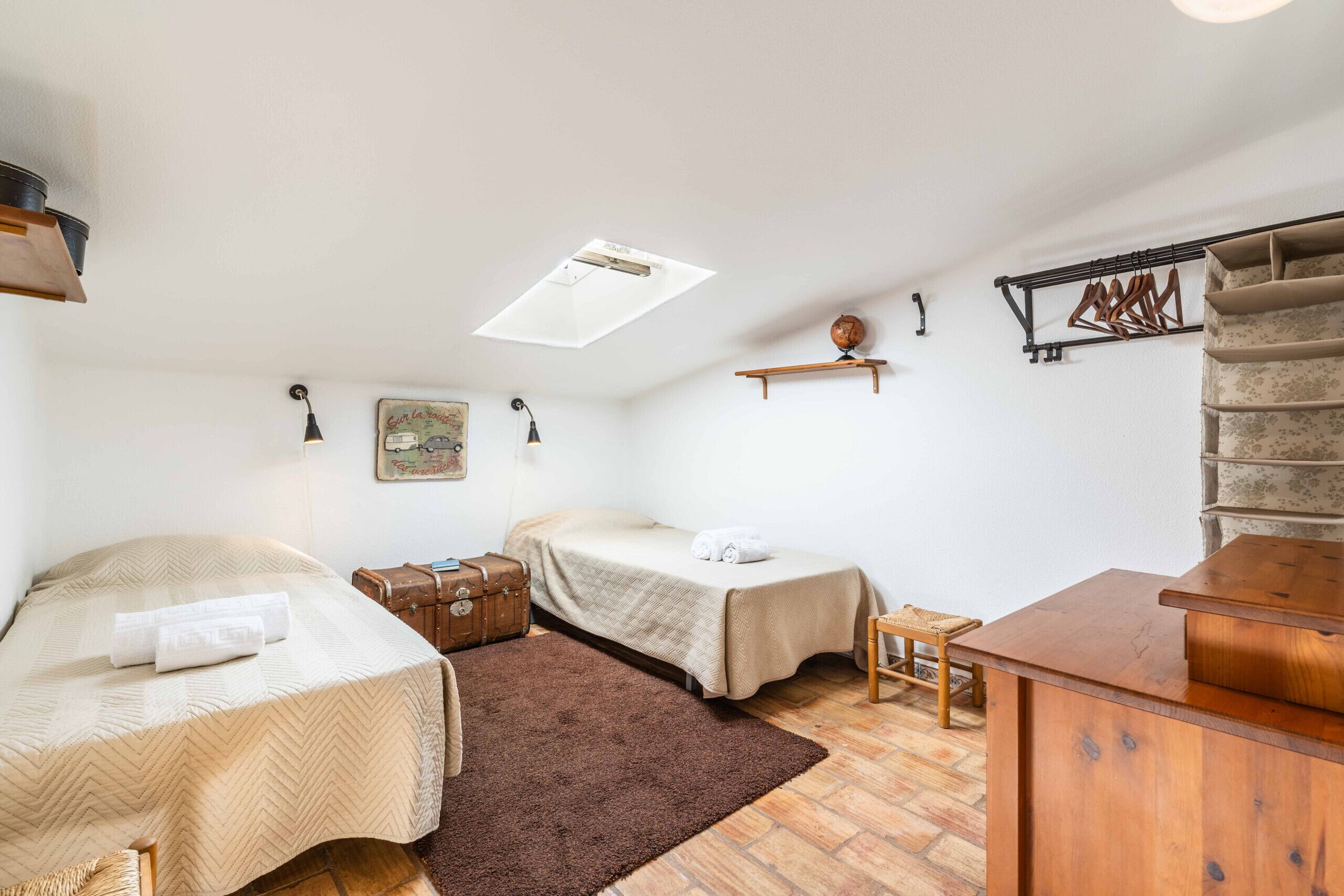 A room with two beds, a wooden dresser, a small table, a hanging coat rack, and a skylight.