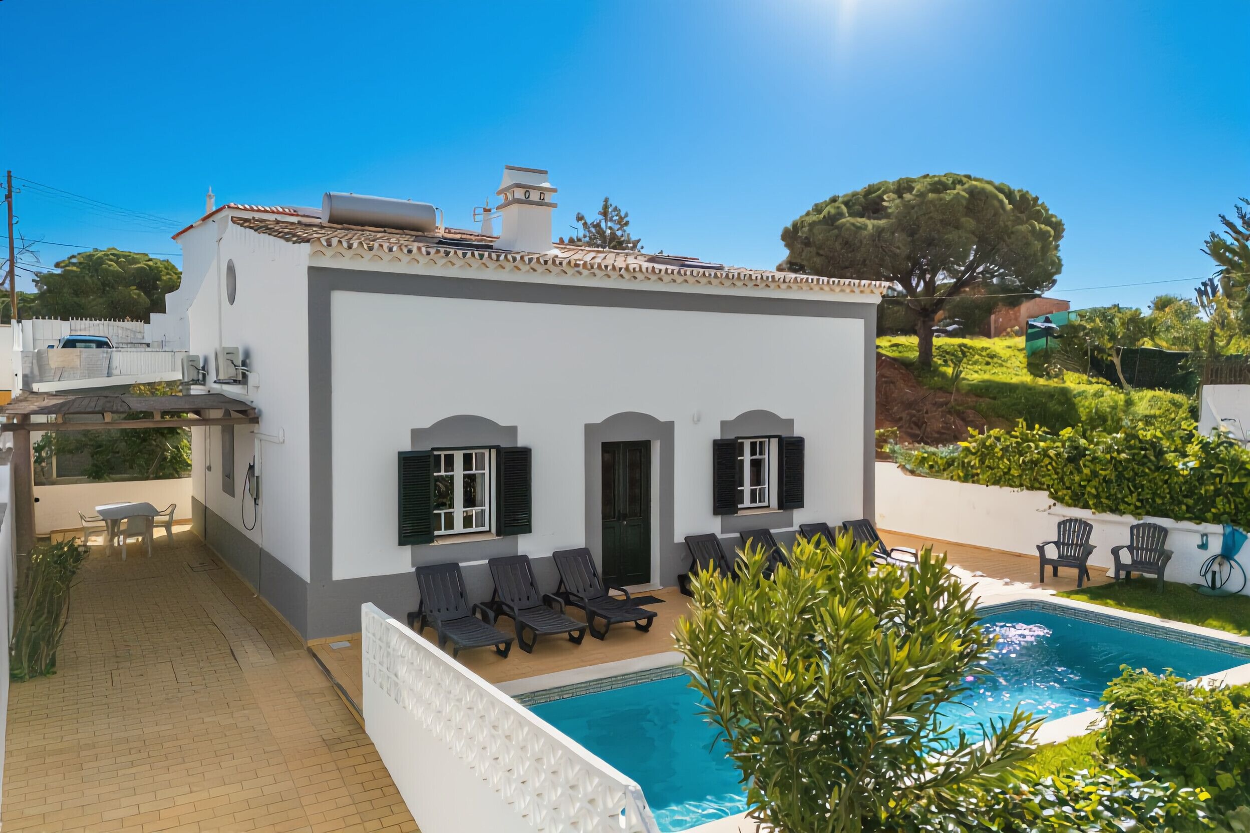 A white building with a swimming pool, outdoor seating, and a garden.