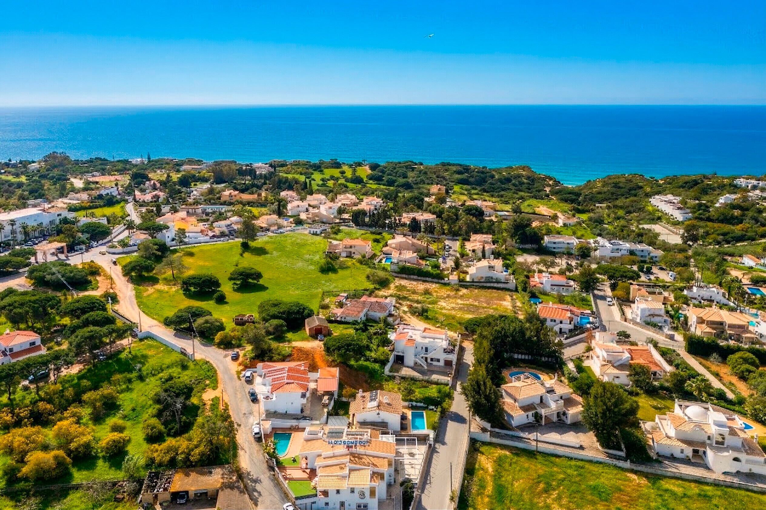 An aerial view of a coastal residential area with houses, roads, and a clear view of the sea.