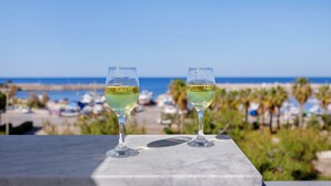Deux verres de vin blanc sur une surface en marbre, avec une vue sur la plage en arrière-plan.