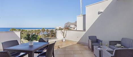 A terrace with a table and chairs, a potted plant, and a view of the sea.