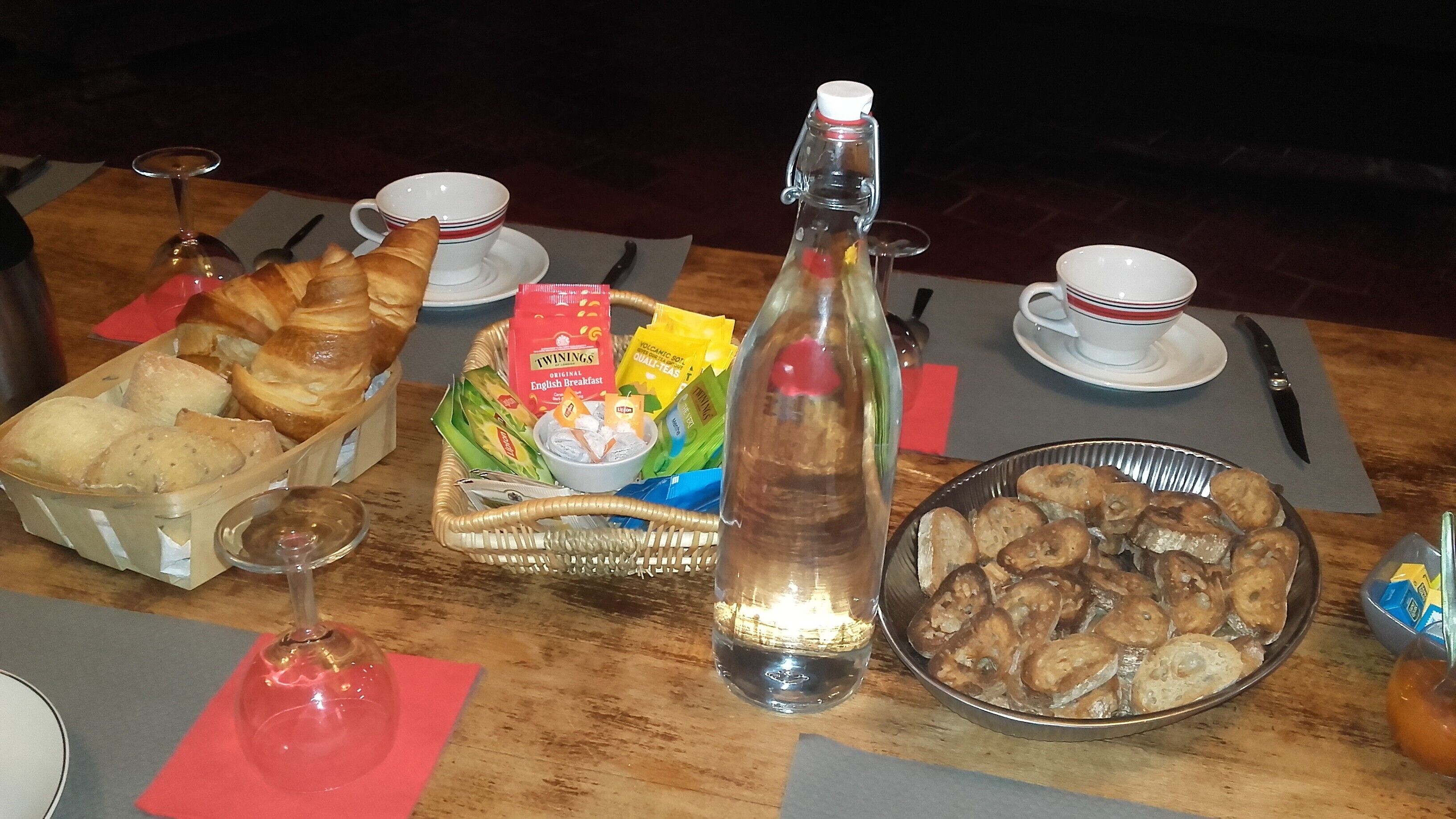 Ein Frühstückstisch mit Brot, Gebäck, einer Flasche und Teebeuteln.