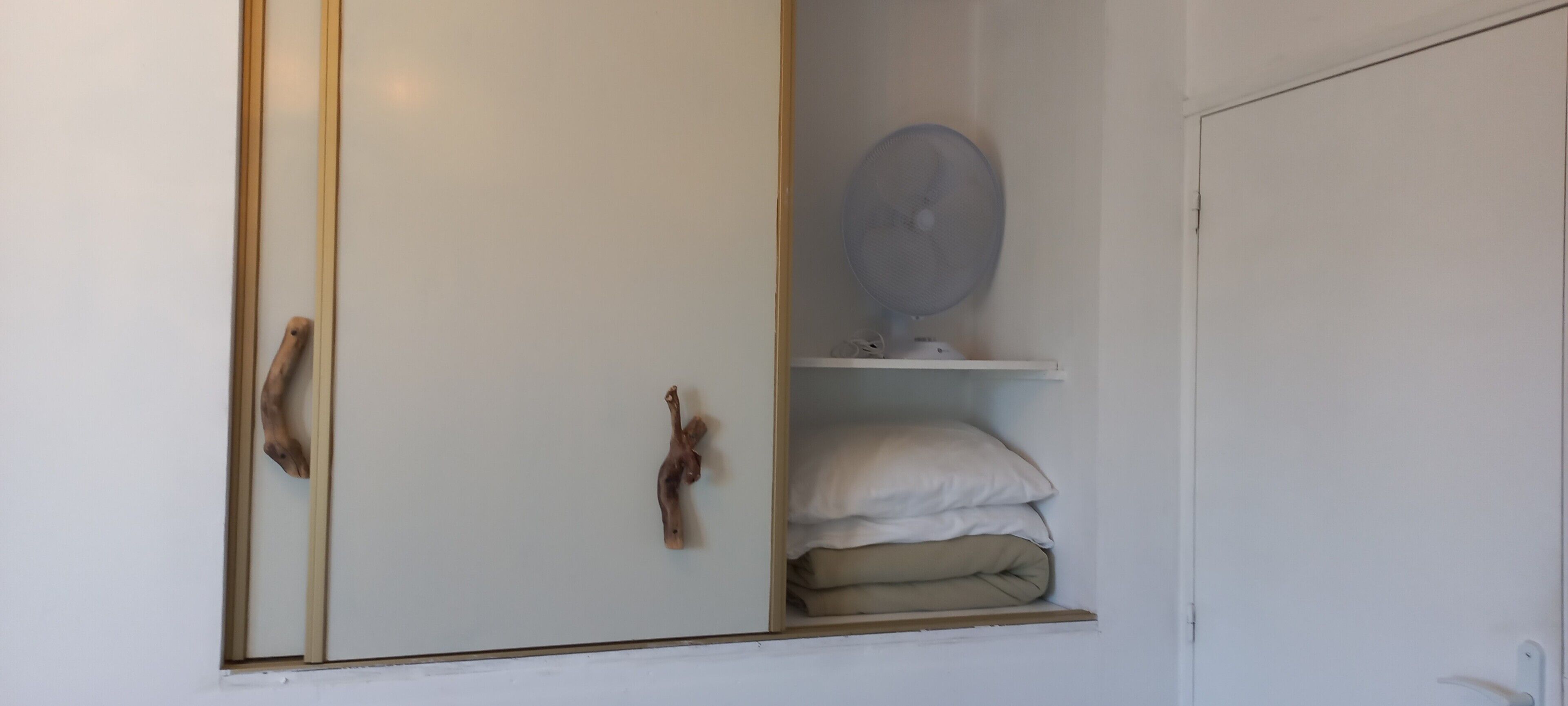 Ein Schrank mit Spiegel, Ventilator und gefalteten Decken.