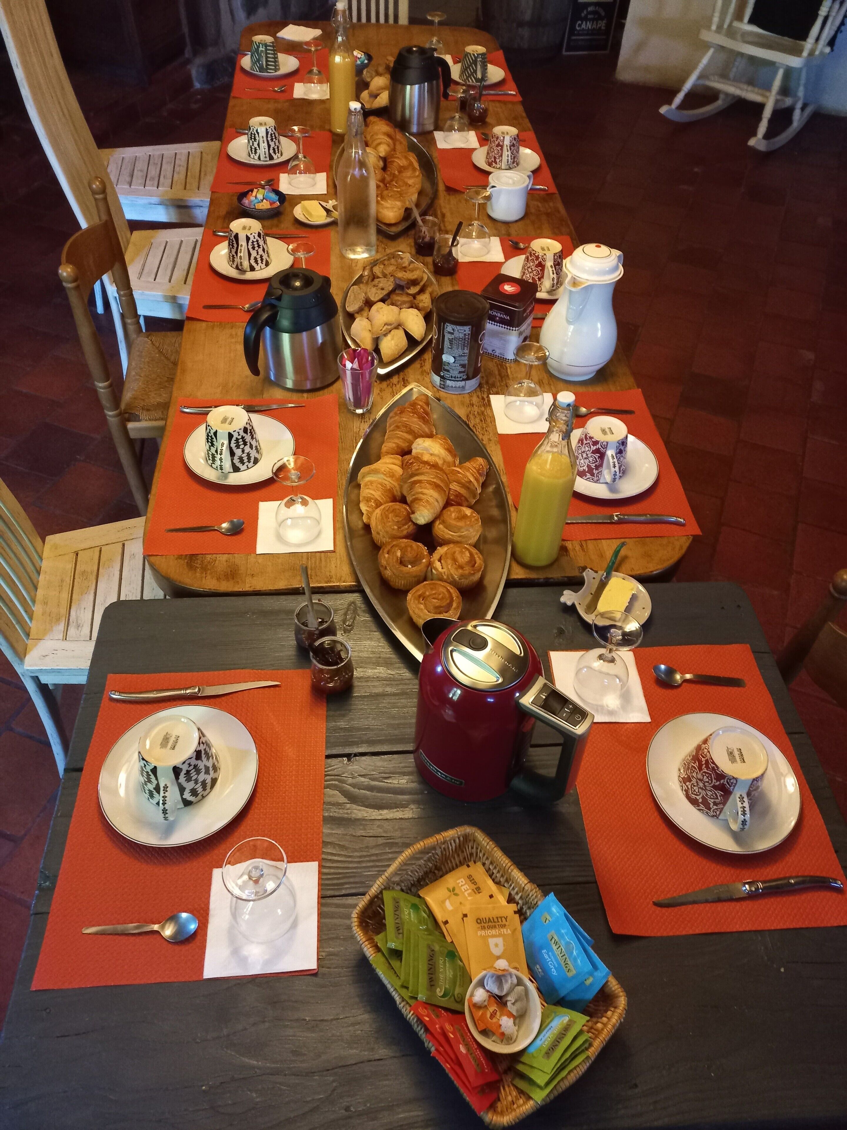 Une table de petit-déjeuner dressée avec des croissants, des pâtisseries et des boissons, entourée de chaises.