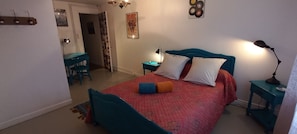 Een slaapkamer met een bed, een bureau en een stoel. Er is een deur die naar een andere kamer leidt.