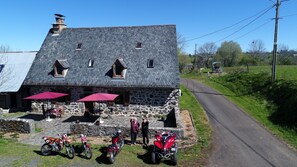 Un edificio de piedra con techo inclinado, mesas al aire libre con sombrillas y motocicletas estacionadas frente a él.