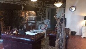 A stone-walled room with leather sofas, a wooden chair, a glass coffee table, and a lamp on a white dresser. - Bed and Breakfast 'Roc' with Shared Terrace and Shared Garden (Saint-Bonnet-de-Salers)