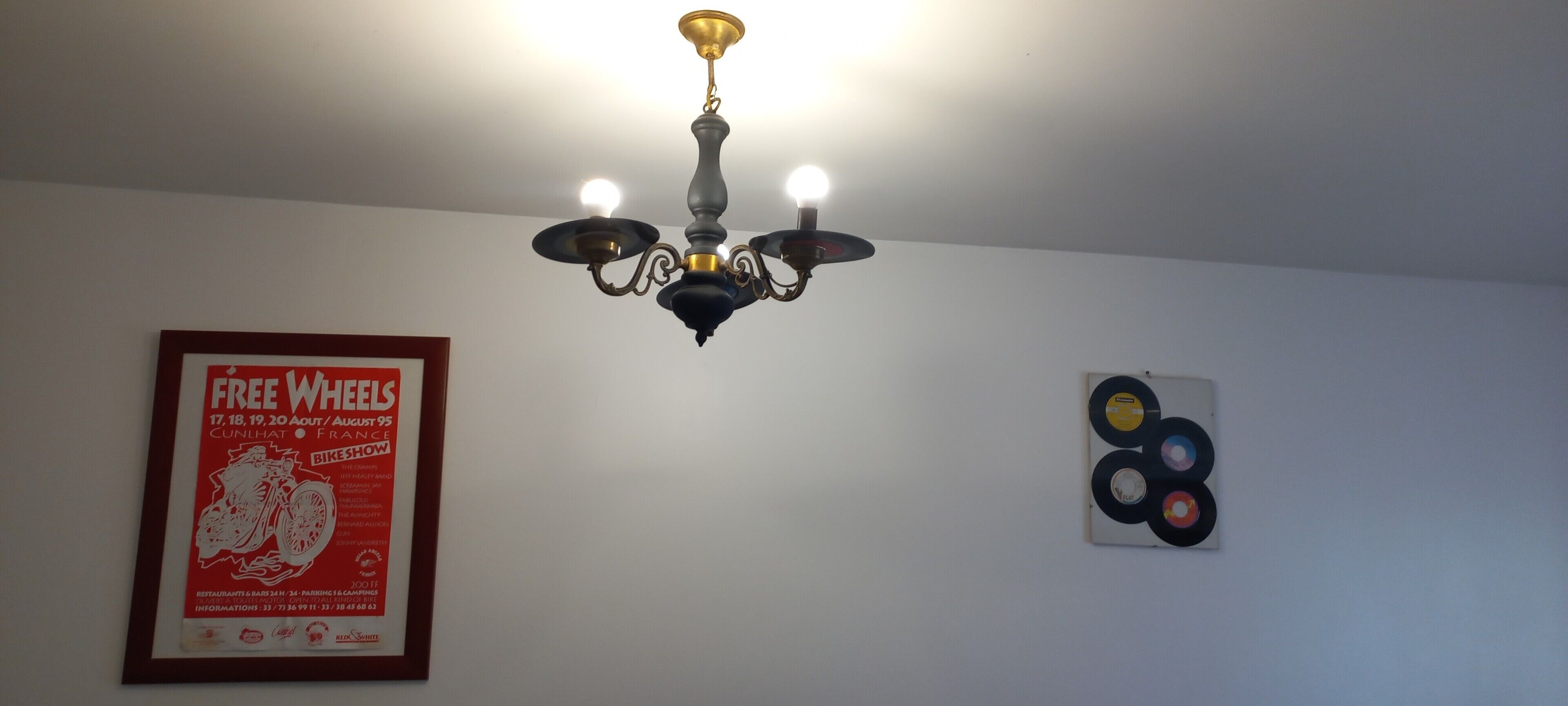 Un lustre à trois lampes, une affiche encadrée accrochée au mur et une œuvre d’art murale représentant un disque vinyle.