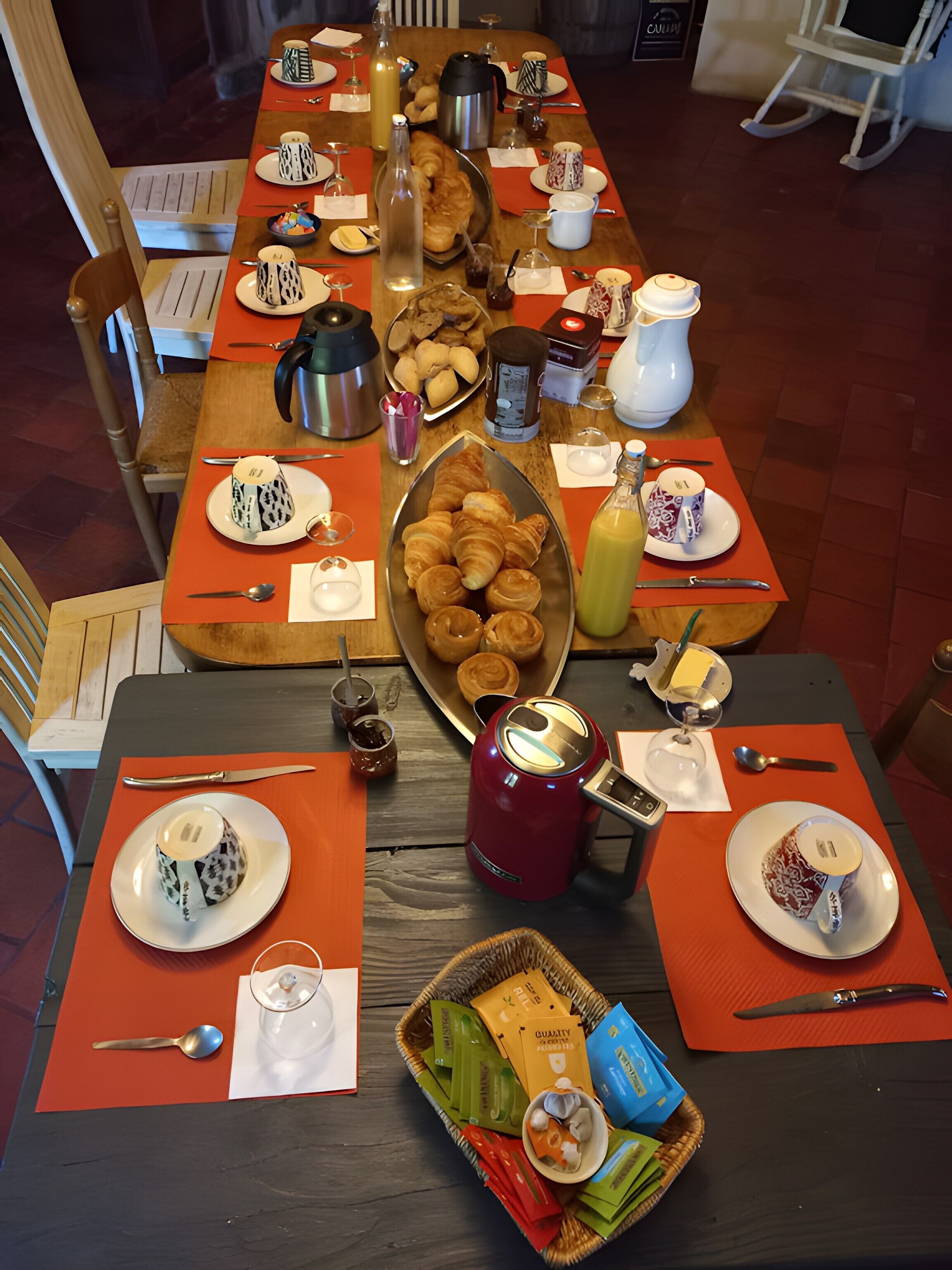 Une table en bois dressée pour le petit-déjeuner, avec des croissants, du café et du thé.