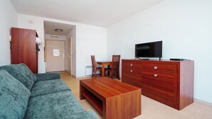 A compact living space with a sofa, a wooden dining table with chairs, a TV on a cabinet, and a door leading to another room. - Small studio for 2 people, close to amenities (Agde)