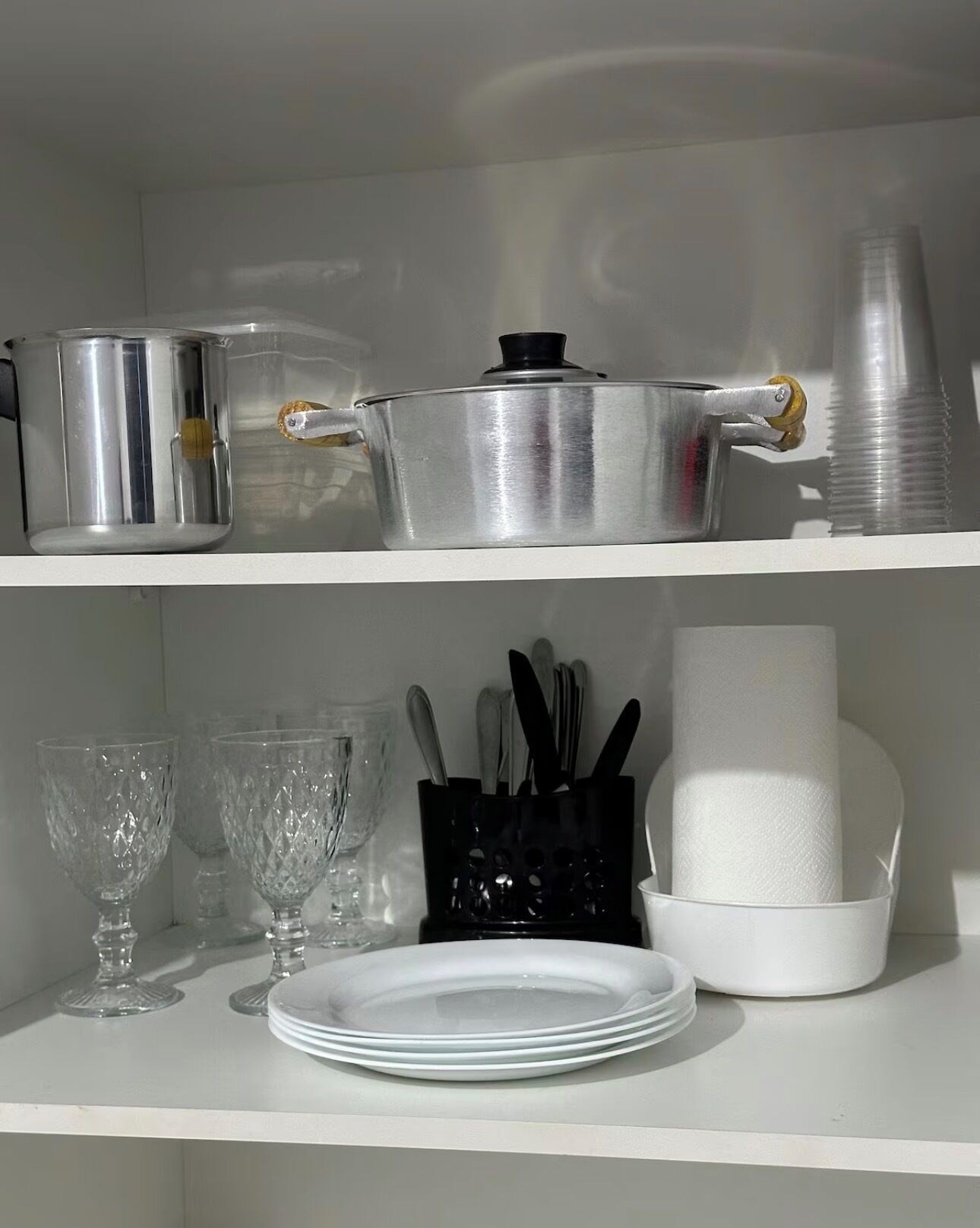 A kitchen shelf with cookware, glassware, and a napkin holder.