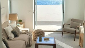 Ein Zimmer mit einer Couch, einem Sessel, einer Lampe und Meerblick durch ein großes Fenster.