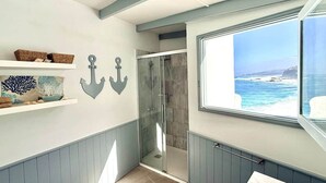 Ein Badezimmer mit Dusche, einem Fenster mit Meerblick und dekorativen Wandankern.