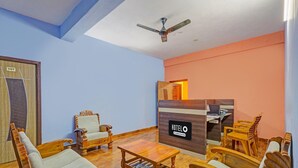 A hotel room with a wooden sofa set, a coffee table, a ceiling fan, and a reception desk with a sign. - Deluxe tad Homes (Sriperumbudur)