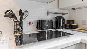 Keittiössä on musta liesi, kahvinkeitin ja vedenkeitin. Astioita on säilytetty telineessä, ja hyllyllä on merkityillä etiketillä varustettuja säilytysastioita.