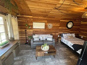 Une chambre confortable, aménagée dans le style d’un chalet, avec un canapé, un lit, une table basse en bois sur laquelle se trouve un panier, et une horloge murale.