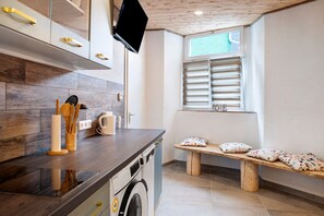 A kitchen with wooden cabinets, a washing machine, a wooden bench with pillows, and a window with blinds. - Apartment 'Carlo' with Wi-Fi (Meßkirch)