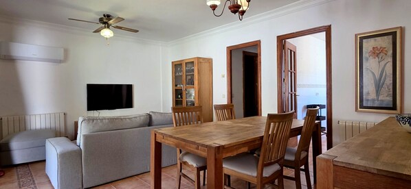 A living room with a sofa, wooden dining table, chairs, a ceiling fan, and a TV.