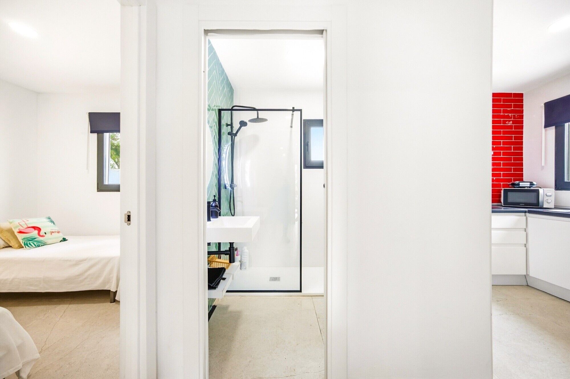 A modern hotel room with a bed, a bathroom with a shower, and a kitchenette.