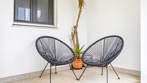 Two black wireframe chairs, a potted plant, and a window on a plain wall.