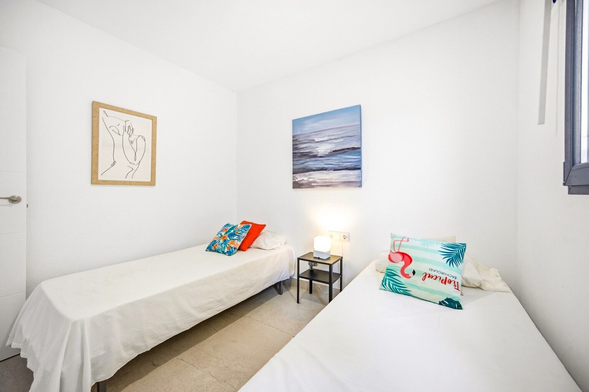 A room with two single beds, a nightstand with a lamp, a framed artwork, and a painting on the wall.