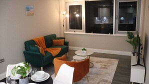 Un salon avec un canapé vert, un fauteuil orange, de petites tables rondes et une plante en pot.