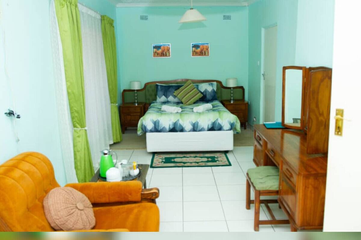 A bedroom with a bed, a desk, a chair, a dresser, and a mirror.