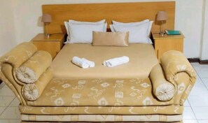 A bed with a patterned bedspread, two pillows, and rolled towels.