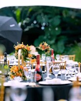 Una mesa dispuesta para un evento formal, con mantel negro, copas de vino y centros de mesa florales.