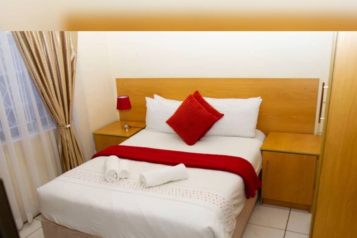 A hotel room with a bed, a nightstand, a lamp, a window with curtains, and a door.