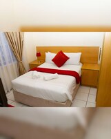 Habitación de hotel con cama, mesita de noche, lámpara, ventana con cortinas y puerta.