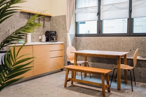 A kitchen with a wooden table and chairs, a coffee machine, and a window with curtains. - Modern Living in Friedrichshain by Sabine (Berlin)