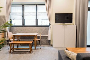 A room with a wooden table and chairs, a television on the wall, a sofa, and a window with curtains. - Modern Living in Friedrichshain by Sabine (Berlin)