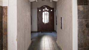 A hallway with a decorative white archway, a wooden door, and tiled flooring.