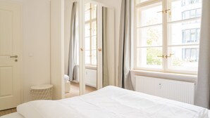 A hotel room with a bed, a window with curtains, a radiator, and a door.