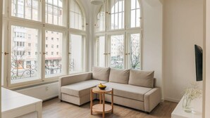 A room with a beige sofa, a small round table with a bowl, large arched windows, and a radiator.